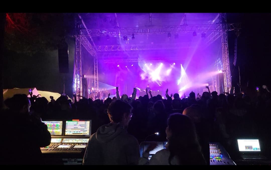 Scène de concert sous les projecteurs violets, public et régie au premier plan